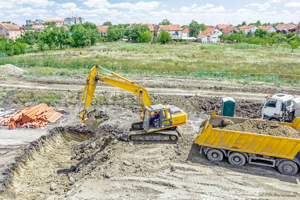 Excavatorul sapă un șanț și încarcă un camion pe clădire — Fotografie, imagine de stoc