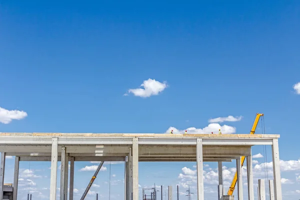 Crane está trabajando en un nuevo edificio, esqueleto de hormigón contra azul — Foto de Stock