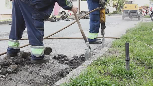 Trabalhador com uma pá recolhe asfalto quebrado atrás jackhammer — Vídeo de Stock