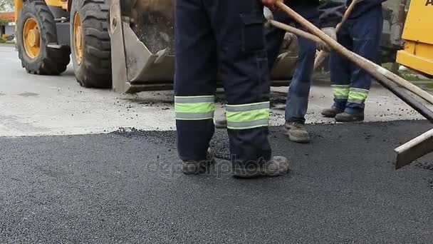 Arbeiter ebnen heißen Asphalt, nachdem er auf dem Boden aufgetragen wurde, Straßenbauarbeiten — Stockvideo