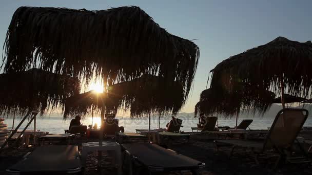 Vista de silueta de sombrillas de paja con tumbonas al lado de la costa — Vídeos de Stock
