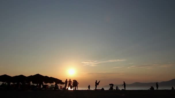 Plan silhouetté du coucher du soleil avec les gens près de la plage — Video