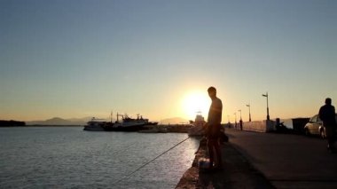 Gün batımında iskelede balık tutan bir çocuk kontrast atış