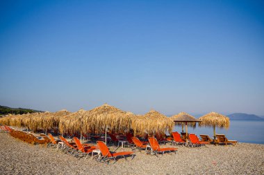 Kıyı şeridi yanındaki plastik şezlong ile thatched şemsiye 