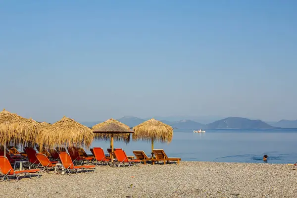 Kıyı şeridi yanındaki plastik şezlong ile thatched şemsiye 