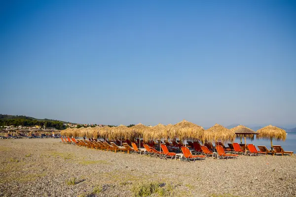 Parasole kryte strzechą z plastikowych leżakach obok wybrzeża — Zdjęcie stockowe