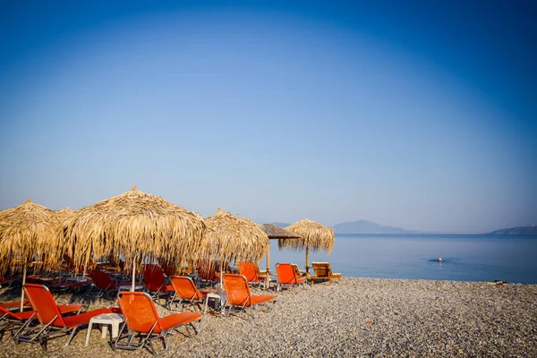 Kıyı şeridi yanındaki plastik şezlong ile thatched şemsiye 