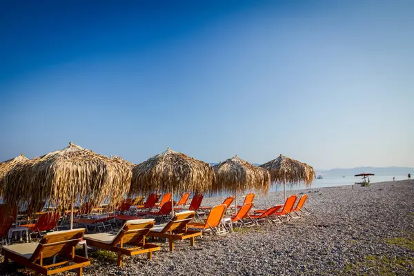 Kıyı şeridi yanındaki plastik şezlong ile thatched şemsiye 