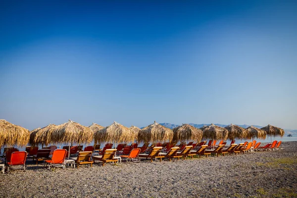 Kıyı şeridi yanındaki plastik şezlong ile thatched şemsiye 