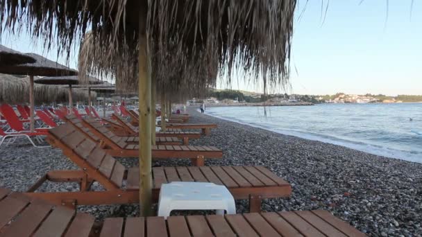 Houten ligstoelen met stro paraplu's om te ontspannen aan het strand — Stockvideo