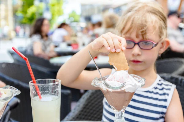Милая девочка в очках ест мороженое в ресторане — стоковое фото