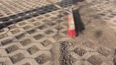 İşçi işçi geniş bir süpürge ile kuru pislik süpürür kırmızı süpürge ile modern parke taşı Temizleme, kentsel mekan temizleme fırçası döşeli.