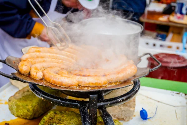 Girando deliziose salsicce succose su piastra barbecue con manico — Foto Stock