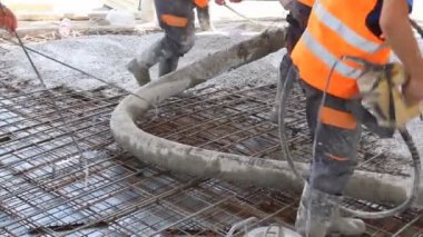 İşçiler beton takviyeli katta büyük inşaat alanı üzerinden yayılıyor. İnşaat İşçileri temel, yapı içinde beton pompa tüp belgili tanımlık doğru yön yönetmenlik yağıyor.