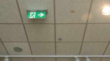 Yeşil acil, yangın çıkış işareti. Standart uluslararası sembolü güvenli çıkış işareti tavandan asılı duruyor. Çıkış acil yeşil Uluslararası Çıkış işaretidir bir kamu Binası.