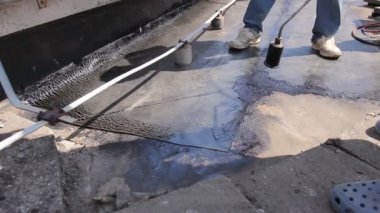 Isıtma ve alev tarafından bitüm yüzeyden gaz Meşalesi erime. İşçi keçe çatı için Bitümlü kapak ayarlar, eritilmiş reçine ahşap aracı ile smear. Yükleme reçine çatı kaplama, ekip çalışması 