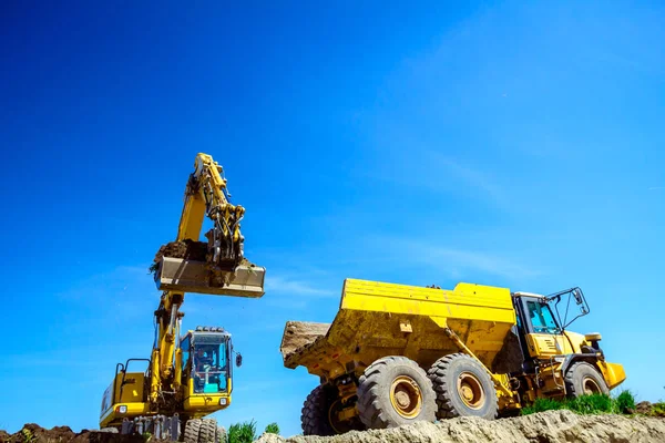 Excavadora está cargando un camión con tierra en el sitio de construcción — Foto de Stock