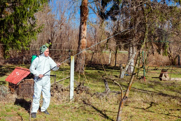 Gardener wearing protective overall sprinkles fruit trees with l — ストック写真