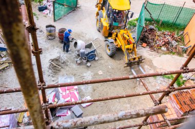 İnşaat alanının üstünde inşaat işçisi mikserde beton yapıyor. Kazı makinesi teslimat için forklift olarak çalışıyor..