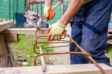 İşçi beton kiriş için takviye çerçeve yapmak için pense kullanarak demir çubuğu tel ile bağlıyor.. 