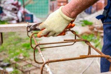 İşçi beton kiriş için takviye çerçeve yapmak için pense kullanarak demir çubuğu tel ile bağlıyor.. 