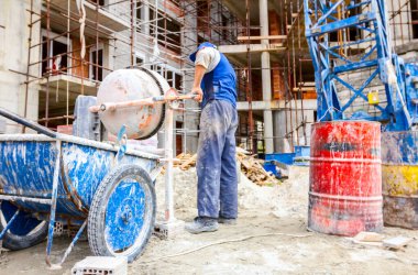 İşçi çimento karıştırıcı betondan el arabası yağıyor.