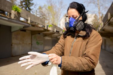 Yüzünde filtre maskesi olan kadın COVID-19 virüsüne karşı korunmak için ellerine lastik eldiven takıyor.. 