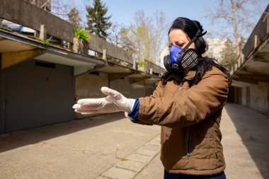 Yüzünde filtre maskesi olan kadın COVID-19 virüsüne karşı korunmak için ellerine lastik eldiven takıyor.. 