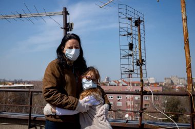 Medya baskısını durdurun. Anne, korkmuş kızını kucaklıyor. Eldivenleri ve maskeleri var. COVID-19 virüsünden korunmak için..