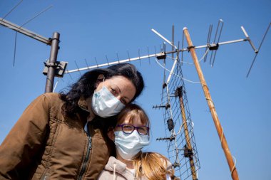 Medya baskısını durdurun. Anne, korkmuş kızını kucaklıyor. Eldivenleri ve maskeleri var. COVID-19 virüsünden korunmak için..