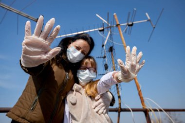 Anne onu korkutan kızını kucaklıyor. Ellerinde tıbbi eldiven ve maskeler var. Elleriyle, hareketleriyle, sosyal mesafeleriyle, COVID-19 virüsüne karşı korunarak Corona 'dan uzak durduğunu gösteriyor..