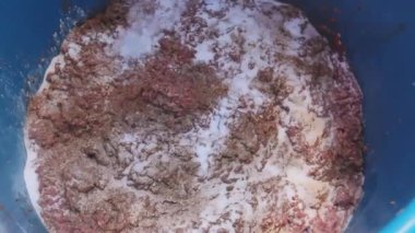 Aşçı, ince plastik bir kasede kıyma üzerine baharat döküyor. Sosis yapmak için açık havada et işliyor..