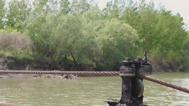 İnsan gücü el yapımı feribotta. İnsanlar, feribotu nehrin karşısına geçirmek için ahşap kollu çelik kabloyu çekiyorlar..