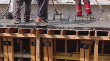 İnşaat işçileri tahta kalıptaki taze betonu güçlendirmek için elektrikli alet, sıkıştırıcı ve kürek kullanıyorlar..