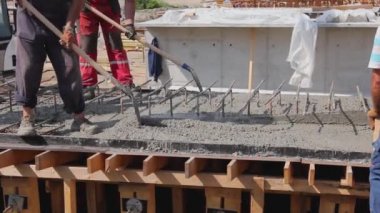 İnşaat işçileri kürek ve mala kullanıyor. Tahta kalıptaki taze betonu takviyeyle hizalamak için..