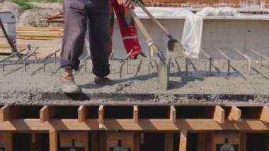 İnşaat işçileri tahta kalıptaki taze betonu güçlendirmek için elektrikli alet, sıkıştırıcı ve kürek kullanıyorlar..