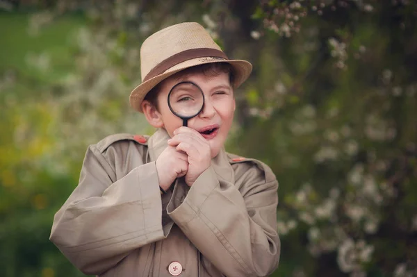 Büyüteçle gülümseyen çocuk doğada dedektifçilik oynuyor.