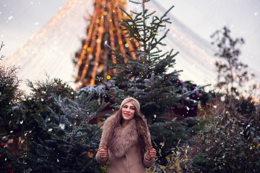 christmas portrait of happy child holding burning sparkler or firework outdoor, snowy winter decorated tree on background. New Year Holidays in city.