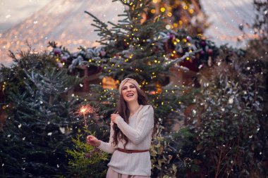 Yanan maytap ya da havai fişek tutan mutlu bir çocuğun Noel portresi, arka planda karlı bir kış ağacı. Şehirde yeni yıl tatili.