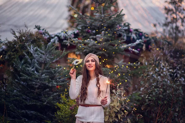 燃える輝きや花火の屋外を保持幸せな女の子のクリスマスの肖像画 背景に雪の冬の装飾された木 市内のお正月 — ストック写真