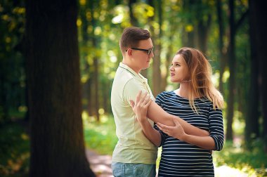 Yakışıklı adam ve güzel hamile karısı parkta yürüyüş için sarılıp gülümsüyorlar.