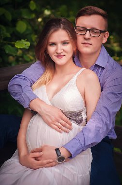 Yakışıklı adam ve güzel hamile karısı parkta yürüyüş için sarılıp gülümsüyorlar.