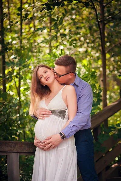 公園での散歩のために抱きかかえて笑顔ハンサムな男と彼の美しい妊娠中の妻 — ストック写真