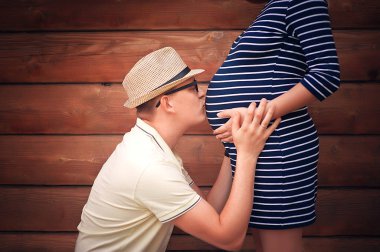 Yakışıklı adam güzel hamile karısının karnını dinliyor ve gülümsüyor.