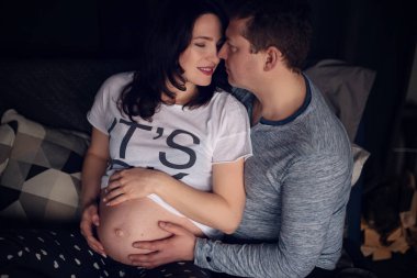 Yakışıklı adam güzel hamile karısının karnını dinliyor ve gülümsüyor.