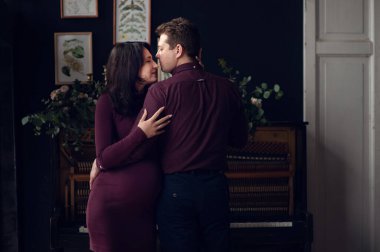 Yakışıklı adam güzel hamile karısının karnını dinliyor ve gülümsüyor.