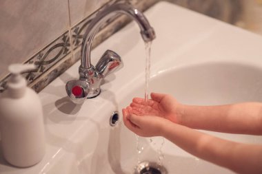 Küçük çocuk banyodaki lavabonun üzerinde ellerini sabunla yıkıyor.