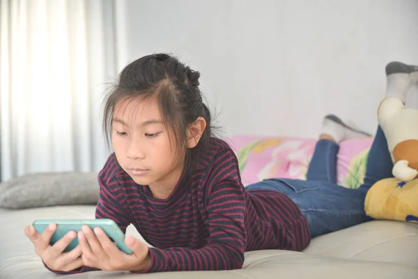 Gelukkig Aziatische kind meisje slimme telefoon kijken op bed thuis. — Stockfoto