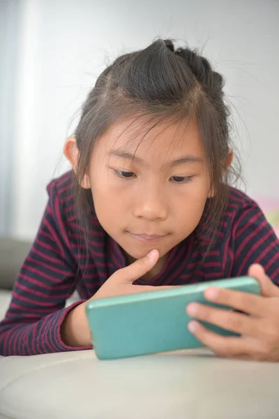 Lyckligt asiatiska barn flicka tittar på smart telefon på sängen hemma. — Stockfoto