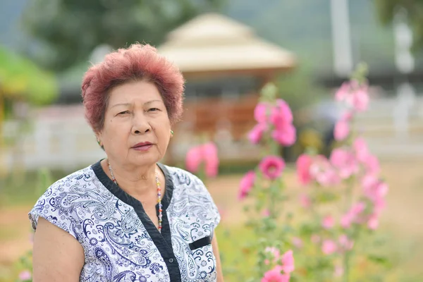 Asiática Senior mujer con flores en el jardín — Foto de Stock